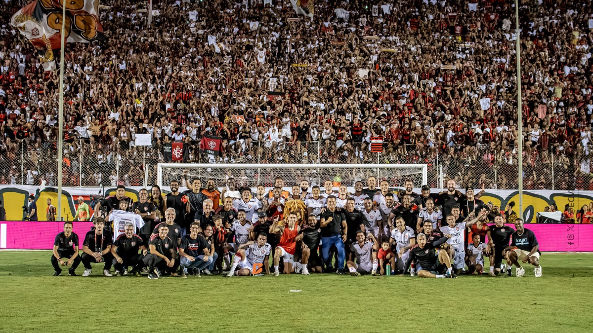 Elenco, direção e comissão técnica do Vitória comemoram permanência na Série A em foto com a torcida ao fundo